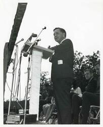 ["Black and white photograph print of Carl Albert giving a speech at the Talimena Drive dedication. George Nigh and Dewey F. Bartlett are also present. July 1970"]