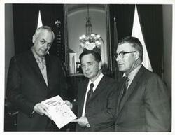 ["Black and white photograph print of Kenneth Grant presents Carl Albert with a copy of the project plan of the Ouachita Mountains Resource Conservation and Development Project. William L. Vaught is also pictured. April 5, 1971"]