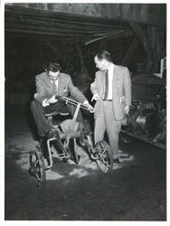 ["Black and white photograph print of Carl Albert and an unidentified man with a farm implement."]