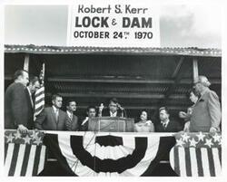 ["Black and white photograph print of George Nigh speaking at the dedication of the W. D. Mayo and Robert S. Kerr locks and dams. Also present are Robert S. Kerr, Jr., Dewey F. Bartlett, Lady Bird Johnson, Ed Edmondson, Carl Albert, Fred Harris, and Lyndon B. Johnson. October 24, 1970"]