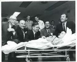 ["Black and white photograph print of Carl Albert visiting with a man on a stretcher."]