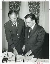 ["Black and white photograph print of Carl Albert with Colonel Vernon Pinkey looking over a map in an office."]