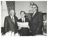 ["Black and white photograph print of Carl Albert, with two unidentified men, viewing a booklet on Talimena Scenic Drive"]
