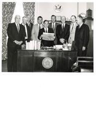 ["Two black and White photograph prints of Carl Albert and a group of eight other unidentified men reading a brochure"]