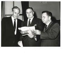 ["Black and white photograph print of Carl Albert (right) with Mike Monroney (left) an  unidentified man (center) going over a ca.1960 Oklahoma travel brochure, Oklahoma vacation Adventureland"]
