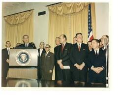 ["Color photograph print of swearing-in ceremonies for Postmaster General John A. Gronouski. Lyndon B. Johnson is speaking.  Also present (from left to right): Chester W. Parrish (Secretary-Treasurer of the National Federation of Post Office Motor Vehicle Employees, AFL-CIO); President Johnson; Don E. Dunn (Executive Vice-President of the United Federation of Postal Clerks, AFL-CIO); Frederick J. O'Dwyer (President of the National Association of Postal Supervisors); Senator A. Willis Robertson of Virginia; Attorney General Katzenbach; Representative John A. Race of Wisconsin; House Majority Whip Hale Boggs (of Louisiana); Representative Clement J. Zablocki of Wisconsin; Carl Albert  (as House Majority Leader); Representative Henry S. Reuss of Wisconsin; and Representative Lynn Stalbaum of Wisconsin.  February 19, 1965"]