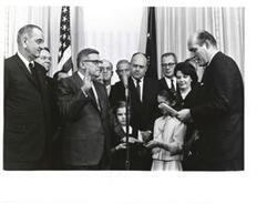 ["Black and white photograph print of Attorney General Nicholas Katzenbach administering the oath of office to Postmaster General John A. Gronouski.  Present in the photograph (from left to right): President Johnson; House Majority Whip Hale Boggs of Louisiana; Postmaster general Gronouski; Representative Lynn Stalbaum of Wisconsin; Senator A. S. Mike Monroney of Oklahoma; Representative Melvin R. Laird of Wisconsin; Secretary of Labor W. Willard Wirtz; Mrs. Gronouski; Secretary of the Treasury C. Douglas Dillon; and Attorney General Katzenbach. February 19, 1965"]