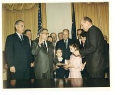 ["Color photograph print of swearing-in ceremonies for Postmaster General John A. Gronouski.  Present in the photograph (from left to right): President Johnson; House Majority Whip Hale Boggs (of Louisiana); Postmaster General Gronouski; Carl Albert (as House Majority Leader); Representative Lynn Stalbaum of Wisconsin; Senator A. S. Mike Monroney of Oklahoma; Representative Melvin R. Laird of Wisconsin; Mrs. Gronouski; and Attorney General Katzenbach."]