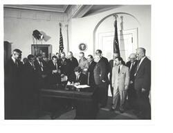 ["Black and White photograph, on stock paper, of John F. Kennedy signing  H.R. 6874, the NASA authorization bill in president's office.  Those present include: Carl Albert, Hubert H. Humphrey, Lyndon B. Johnson, and Robert S. Kerr."]