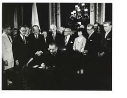 ["Black and White photograph of Lyndon B.  Johnson signing a bill in the president's office.  Those present include:  Hubert Humphrey, John W. McCormack, and Carl Albert."]