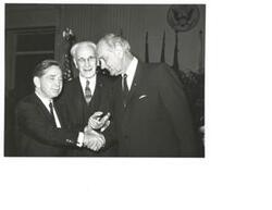 ["Black and White photograph of Lyndon B.  Johnson shaking Carl Albert's hand with House Speaker John McCormack in the background"]
