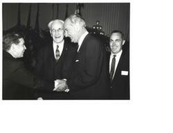 ["Black and White photograph of Lyndon B.  Johnson shaking Carl Albert's hand with House Speaker John McCormack (in the background), and Fred Mutz (on the right) (in Representative  Howard's office)."]