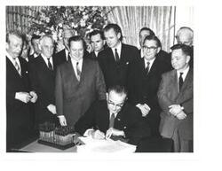 ["Black and white photograph, on stock paper, of Lyndon B. Johnson signing the tax bill in the president's office. Those pictured include:  Carl Albert, Everett M. Dirksen, Russell B. Long, John McCormack, and Wilbur D. Mills. Handwritten message identifying event, by unknown author, on back of photo."]