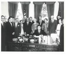 ["Black and white photograph, on stock paper, of John F. Kennedy signing a bill  in president's office.  Carl Albert, Vice-President Lyndon Johnson, and others present."]
