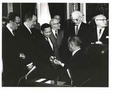 ["Black and white photograph of Lyndon B. Johnson giving out pens for the signing of the Voting Rights Act of 1965. Hubert Humphrey, John W. McCormack, and Carl Albert are present."]