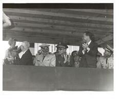 ["Black and white photograph of Carl Albert and some military officers on a speaker's platform."]