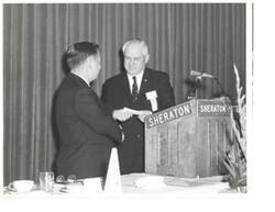 ["Black and white photograph of Carl Albert receiving a check at a VFW dinner."]