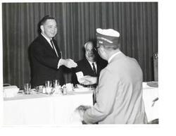 ["Black and white photograph of Carl Albert at a VA dinner receiving a cash donation."]