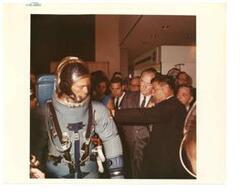 ["Color photograph of Richard S. Johnston, chief of crew systems division, explains the design and function of the Apollo space suit to Hubert H. Humphrey. Carl Albert is in background. Fred Harris is also pictured. July 13, 1965 Manned Spacecraft Center, Houston, Texas.  Jack Mays, of NASA's Crew Systems Division, is demonstrating the spacesuit in the photo."]