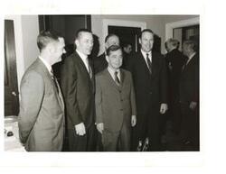 ["Black and white photograph of Carl Albert with a group of unidentified men (Apollo space photo section; probably astronauts). John W. McCormack in background."]