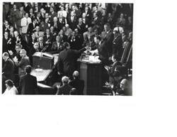 ["Black and white photograph of a group of men in the House chamber. Carl Albert, Gerald Ford, and Richard M. Nixon are pictured."]