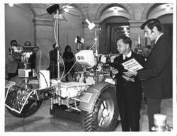 ["Black and white photograph of Carl Albert with unidentified man looking at the lunar rover."]