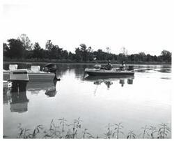 ["Black and white photograph of several fishing boats on a lake."]
