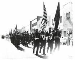 ["Black and white photograph of a parade in McAlester, Oklahoma on Armed Forces Day. Carl Albert and Henry Bellmon are pictured in 3845"]