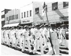 ["Black and white photograph of a parade in McAlester, Oklahoma on Armed Forces Day. Carl Albert and Henry Bellmon are pictured in 3845"]
