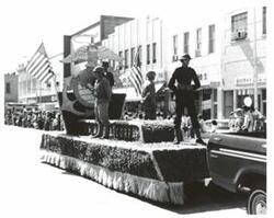 ["Black and white photograph of a parade in McAlester, Oklahoma on Armed Forces Day. Carl Albert and Henry Bellmon are pictured in 3845"]