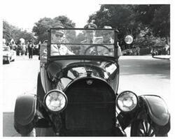 ["Black and white photograph of a car in a parade carrying Carl Albert, Henry Bellmon, Rear Admiral Christman, and Captain Chambliss in McAlester, Oklahoma on Armed Forces Day. 1974"]