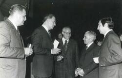 ["Black and white photograph print of several men talking during the House delegation trip. August 1975"]
