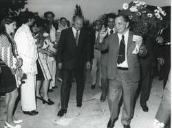 ["Black and white photograph print of Carl Albert holding flowers and walking with some men during the House delegation trip to USSR, Romania and Yugoslavia. August 1975"]