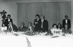 ["Black and white photograph print of Carl Albert and Mary Albert seated at a dinner table with several others. House delegation trip. August 1975"]