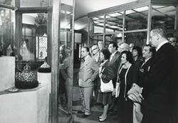 ["Black and white photograph print of Carl Albert and Mary Albert with others looking at an exhibit. House delegation trip. August 1975"]