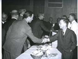 ["Black and white photograph of banquet in McAlester, Oklahoma on Armed Forces Day. 1967 Carl Albert is shaking hands with unidentified man."]