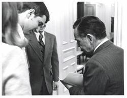 ["Black and white photograph of Carl Albert with a small group, autographing a document."]