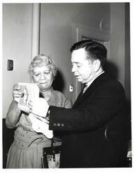 ["Black and white photograph of Carl Albert with a woman looking through the book, \"Up From Slavery.\""]