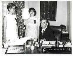 ["Black and white photograph of Carl Albert at his desk with two women from the Oklahoma Journal."]