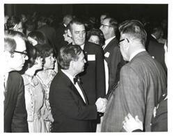 ["Black and white photograph of Carl Albert shaking hands in the midst of a group. Mary Albert and Mary Frances Albert are also present."]