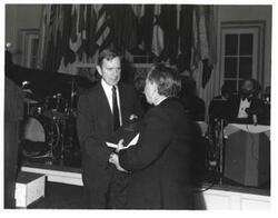 ["Black and white photograph of Carl Albert and Dewey F. Bartlett holding a book and shaking hands. American Revolution Bicentennial Ball in Oklahoma. October 2, 1976"]