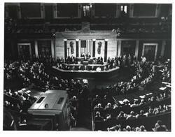 ["Black and white photograph of an astronaut speaking to members of Congress."]
