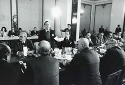 ["Black and white photograph print of Carl Albert, Robert Michel, and several others seated at a conference table. House delegation trip. August 1975"]