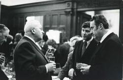 ["Black and white photograph print of three unidentified men speaking to one another. House delegation trip. August 1975"]