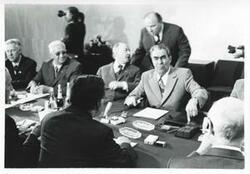 ["Black and white photograph print of Carl Albert, Leonid Brezhnev, and others seated at a conference table during the House delegation trip. August 1975"]