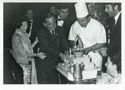 ["Black and white photograph print of Carl Albert and Mary Albert at an unidentified function. Albert is cutting a cake. House delegation trip. August 1975"]