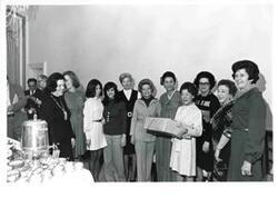 ["A group of women at a farewell party. Mary Albert is holding a gift and Mrs. Dong Jo Kim is standing to her right."]