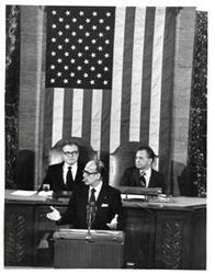 ["Valery Giscard D'Estaing (French president) is speaking before Congress. Nelson A. Rockefeller (left) and Carl Albert (right) are seated behind him."]