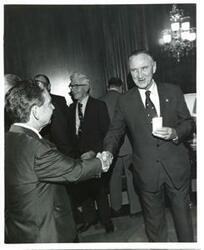 ["Carl Albert shaking hands with Mike Mansfield at the Roz Wyman luncheon."]