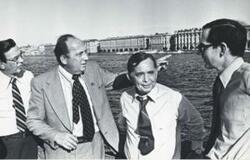 ["Black and white photograph print of Carl Albert, Edward Boland, and two other men standing outside by a large body of water."]